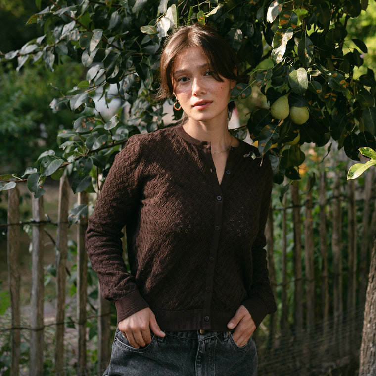 Frau trägt die Pointelle Strickjacke Rieke in Braun mit Jeans, im Garten