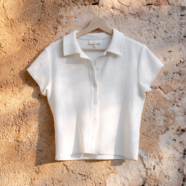 Bluse Aila in Natur, Flatlay am Kleiderbügel vor Steinwand