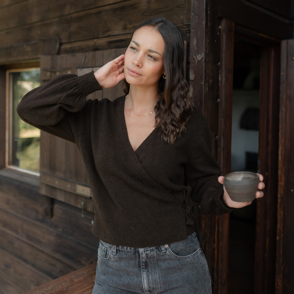 Wickelcardigan Mona, Nahaufnahme mit Tasse in der Hand vor dunkler Holzwand