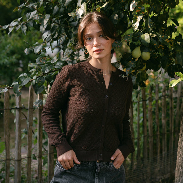 Frau trägt die Pointelle Strickjacke Rieke in Braun mit Jeans, im Garten