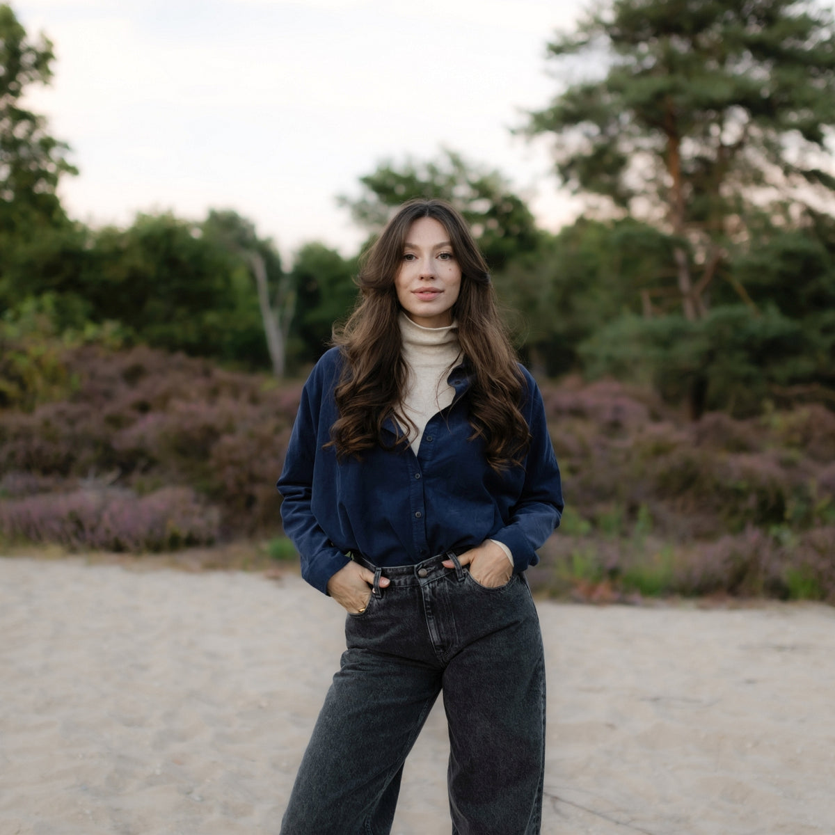Frau trägt die Cordbluse Ruby in Marineblau zu einem cremefarbenen Rollkragenpullover und dunkler Jeans